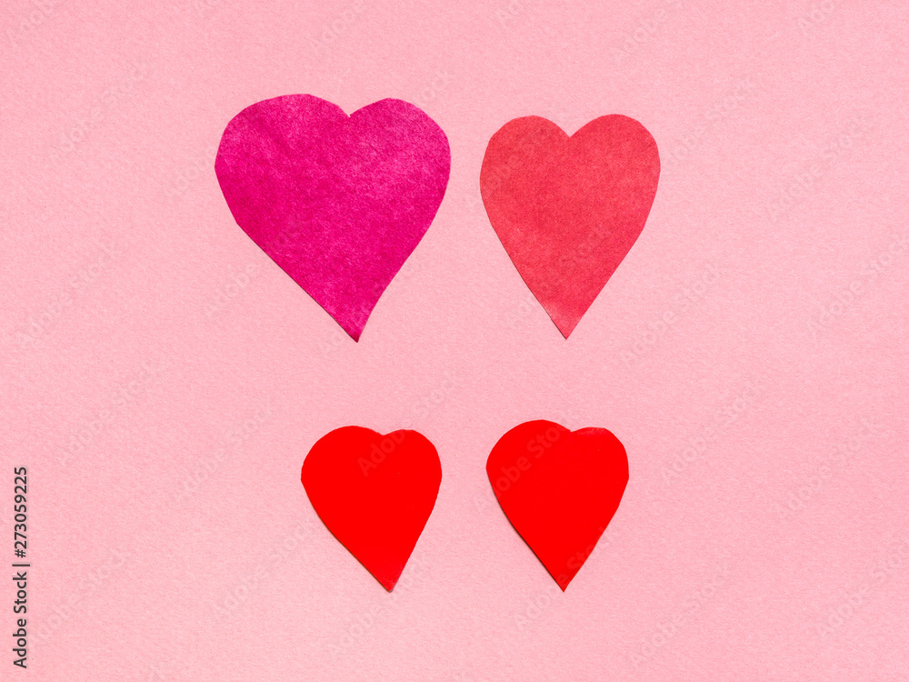 four various hearts cut from red papers on pink