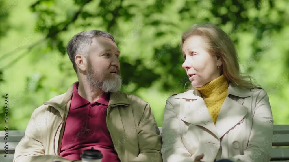 Beautiful senior couple relaxing on bench in park and talking. Mature spouses discussing outdoors Beautiful senior couple relaxing on bench in park and talking. Mature spouses discussing outdoors