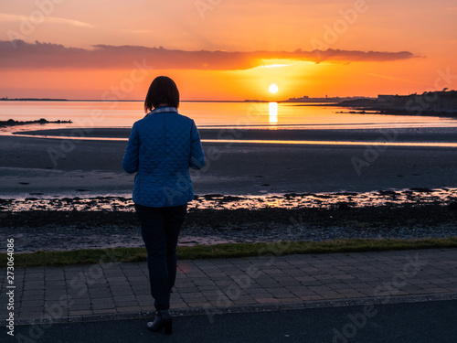 Woman looking at sunset over Galway bay, Rich orange color. Ballyloughane beach. Salthill silhouette.