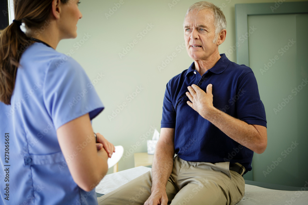 Mature man holds hand to chest and looks at woman doctor Mature man holds hand to chest and looks at woman doctor