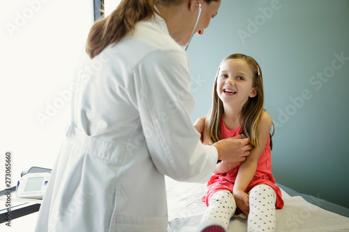 Woman doctor holds stethoscope to young girl's chest