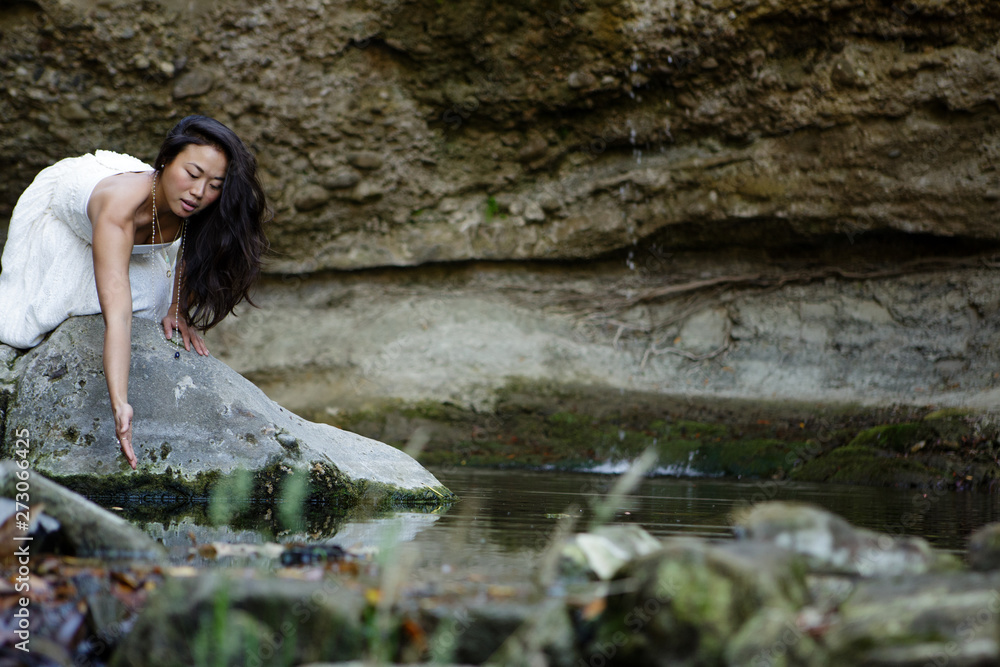 Young woman leaning over rock to touch water Young woman leaning over rock to touch water