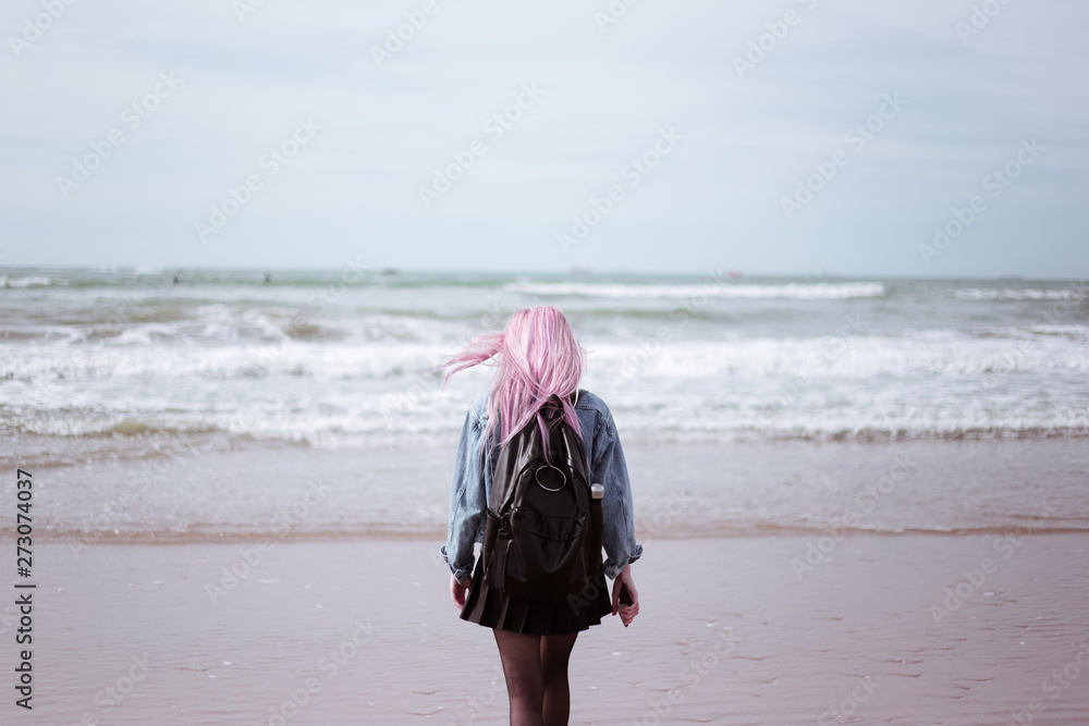 young girl with pink hair with black backpack admiring the sea