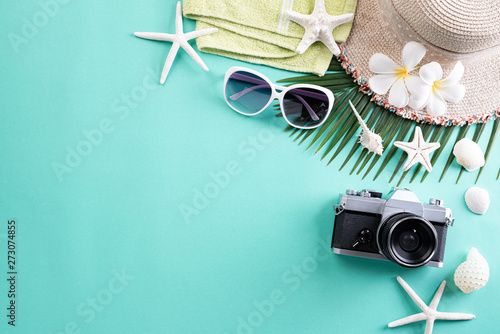 Beach accessories retro film camera, sunglasses, flip flop starfish beach hat and sea shell on green pastel background for summer holiday and vacation concept.