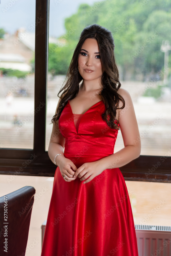 Beautiful young girl in a red dress posing in front of a big window in the restaurant. Fashion and beauty concept. Close up, selective focus Beautiful young girl in a red dress posing in front of a big window in the restaurant. Fashion and beauty concept. Close up, selective focus