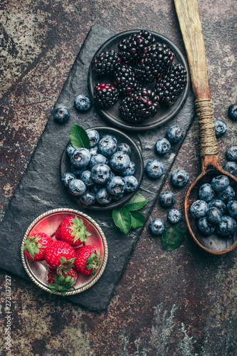 Fresh berries with raspberries, blueberries, blackberries in bowl on a stone stand on a dark metal background.