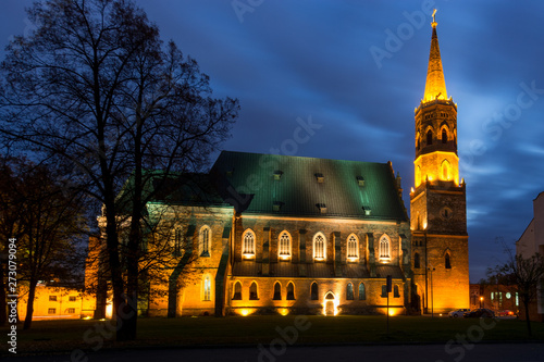 Monumentalna gotycka kolegiata z cegły oświetlona nocą, szeroki kadr na architekturę sakralną, Głogów