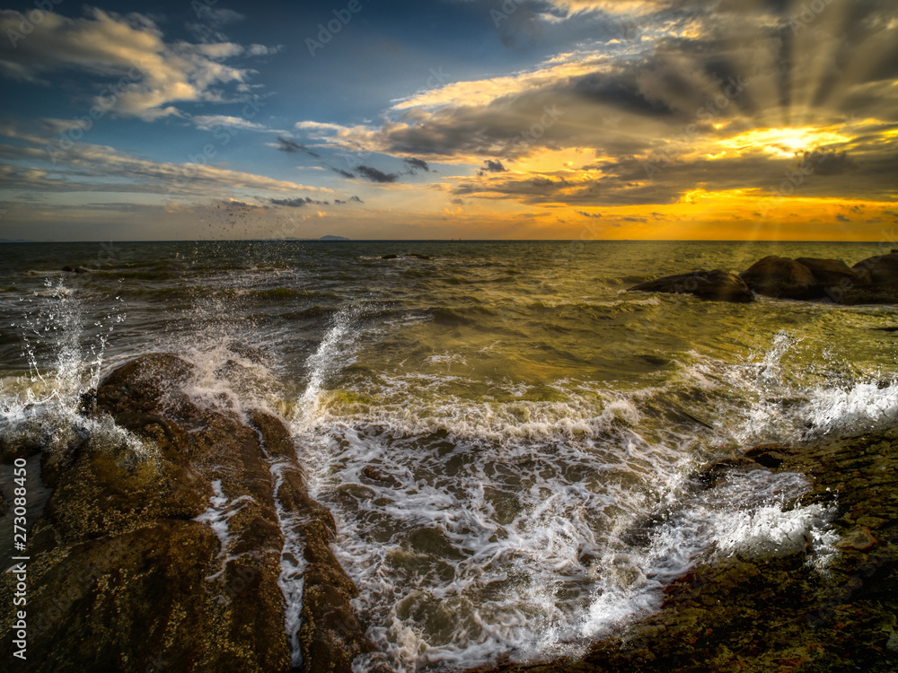 Splashes from the waves bumping against the rocky shore on sunset.