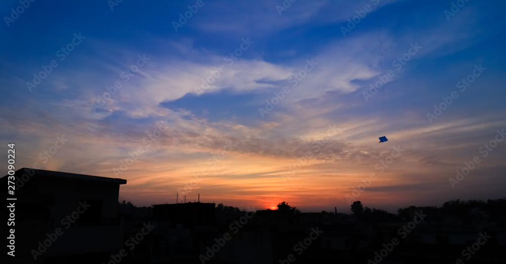 Silhouette of a kite flying in the open sky over a city in summer season, with a beautiful sunset in the background 