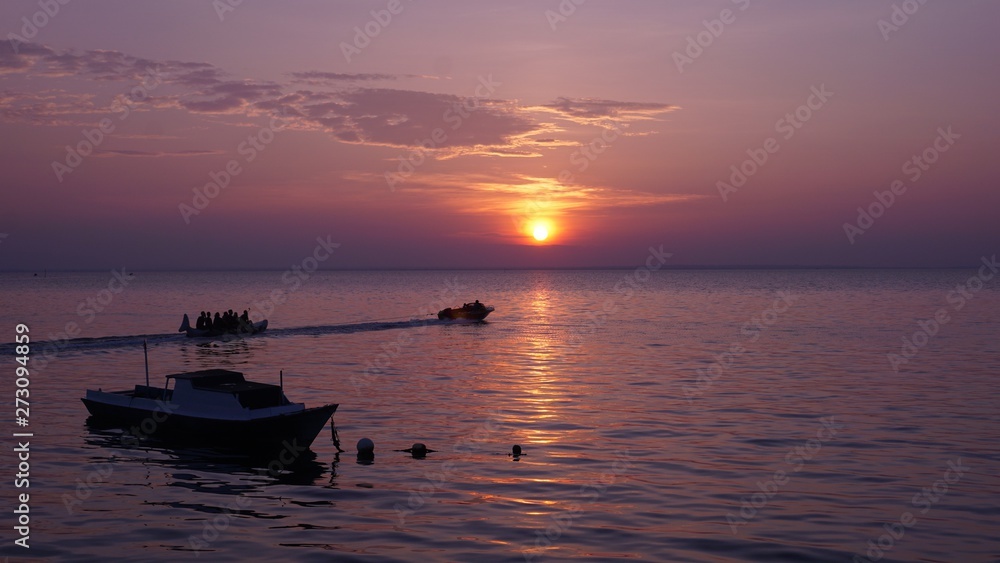 Two boats and banana boat at sunset on the purple beach