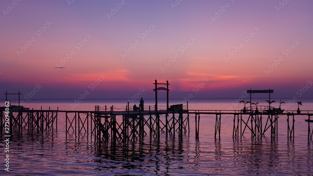 Two silhoutte people on the bridge on the beach at sunset with a purple sky