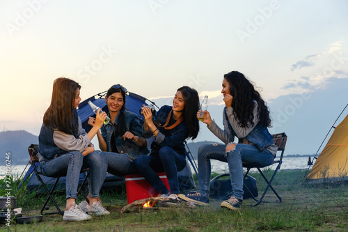 Asian women sit at a party in the middle of the forest near the river and hold a bottle of beer in their hands.