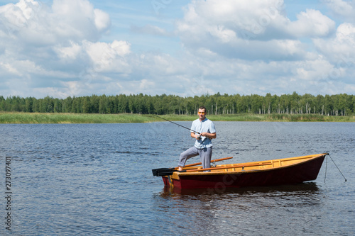 a man stands in a wooden boat in the middle of the lake and fishing for spinning