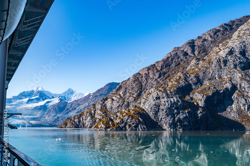 Rocky mountain range in Glacier Bay Alaska with ice/snow covered, broken icebergs floating, reflection in water. Scenic nature tour sailing through the inlet basin in the National Park and Preserve.