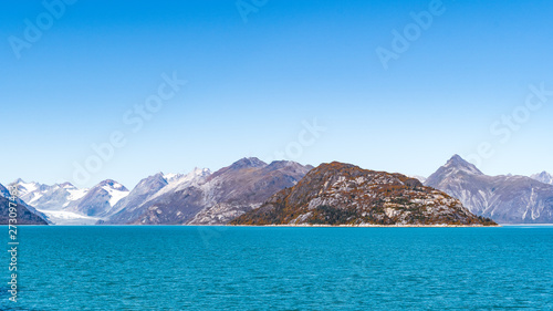 Rocky mountain range in Glacier Bay, Alaska, with ice/snow covered mountains in background. Scenic nature tour sailing through the inlet basin in the National Park and Preserve.