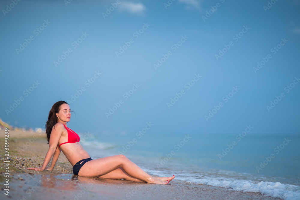 portrait of brunette girl with long hair in red bikini in full length sunbathing on sandy beach