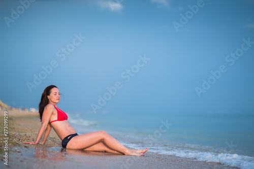 portrait of brunette girl with long hair in red bikini in full length sunbathing on sandy beach
