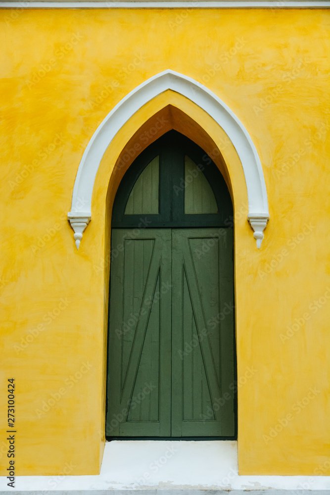 Fototapeta premium an arched green wooden door decorate with white stucco arch on the top in the yellow fresco plaster cement wall finishing