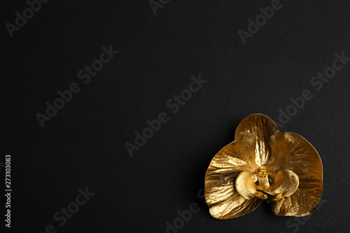 Gold decorative orchid flower on black background, top view. Space for text