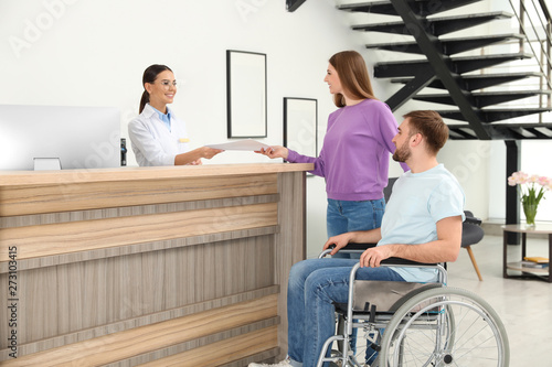 Professional receptionist working with woman and handicapped man at desk in clinic