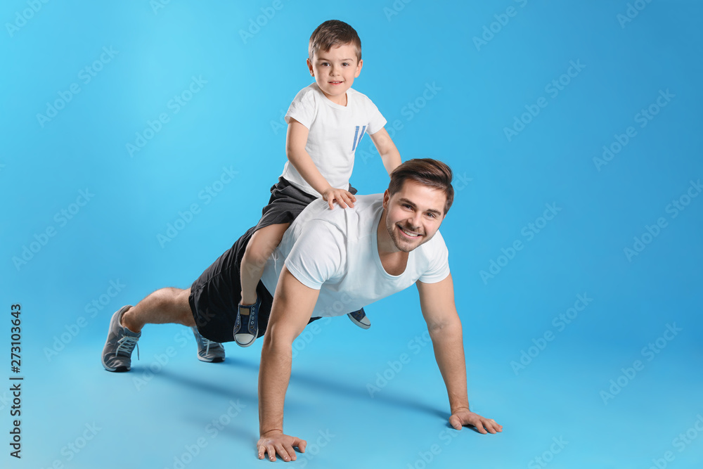 Dad doing push-ups with son on his back against color background