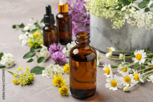 Composition with bottles of essential oils with flowers on grey table