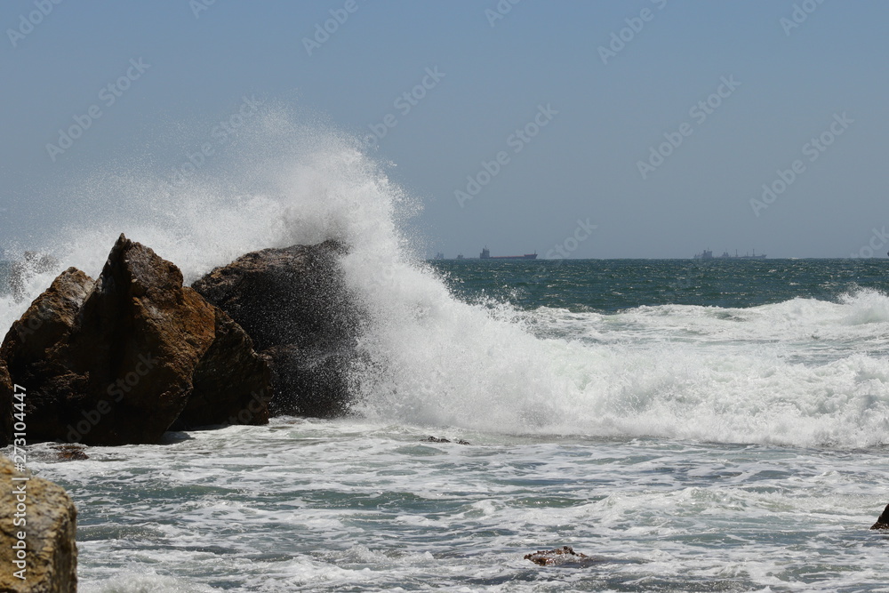 Big storm waves hitting the coastal rocks of the sea. Sunny windy day, blue sky. Splashes and foam. Storm landscape.