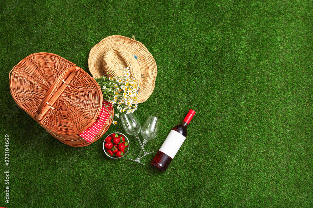Naklejka premium Flat lay composition with picnic basket, wine and strawberries on grass, space for text