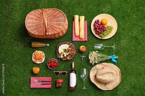 Fototapeta Flat lay composition with picnic basket and products on green grass