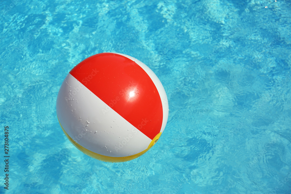 Colorful beach ball floating in swimming pool on sunny day. Space for text