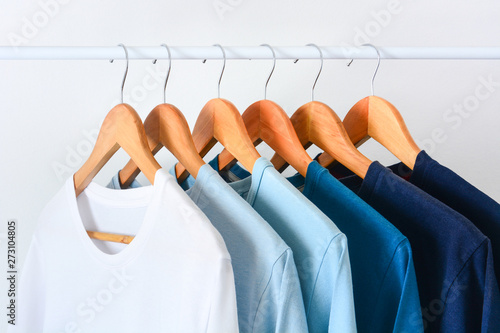 close up collection shade of blue tone color t-shirts hanging on wooden clothes hanger in closet or clothing rack over white background