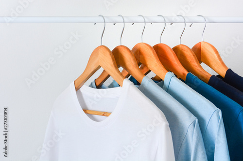 close up collection shade of blue tone color t-shirts hanging on wooden clothes hanger in closet or clothing rack over white background with copy space
