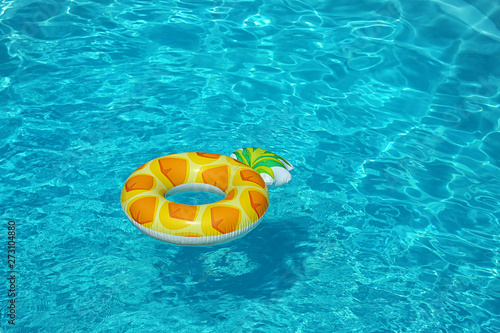 Bright inflatable pineapple ring floating in swimming pool on sunny day. Space for text