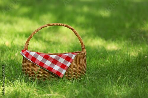 Wicker basket with blanket on green grass in park, space for text. Summer picnic