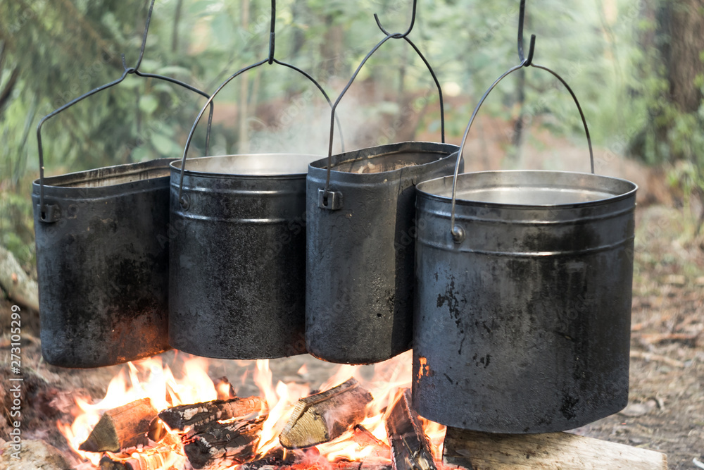 Four tourist boilers, cooking pots in the woods on fire. Campsite with smoke and sunshine Four tourist boilers, cooking pots in the woods on fire. Campsite with smoke and sunshine