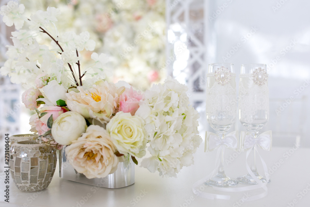 Festive concept of white wedding. Flower arrangement of artificial bouquet on the table. Glasses for the bride and groom. Festive concept of white wedding. Flower arrangement of artificial bouquet on the table. Glasses for the bride and groom.