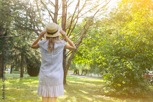 Stylish hipster girl with a straw hat  is standing outdoors. Happy woman in blue dress.  Travel holiday concept. Summer lifestyle photo. Shades of sun and trees. © Vadym