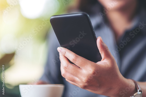 Closeup image of a woman holding and using mobile phone with coffee cup on wooden table in cafe