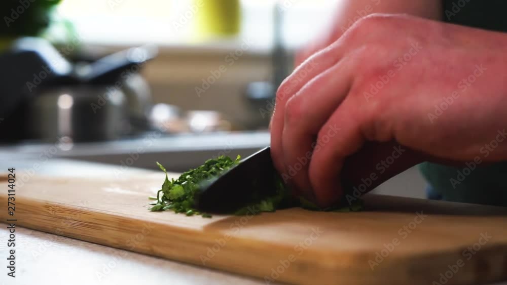 Young male chef is chopping parsley on a wooden chopping board, preparing a vegetarian and vegan meal. Creating a dish for a healthy diet. Young male chef is chopping parsley on a wooden chopping board, preparing a vegetarian and vegan meal. Creating a dish for a healthy diet.
