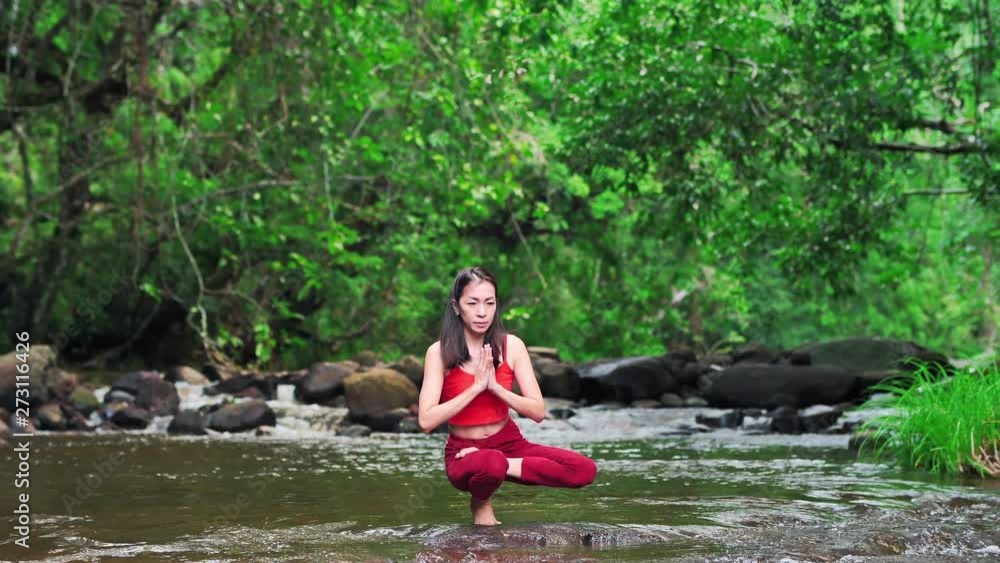 Asian woman practicing or doing yoga at the waterfall. Beautiful Landscape, Natural background, Thailand. Slow motion waterfalls. Asian woman practicing or doing yoga at the waterfall. Beautiful Landscape, Natural background, Thailand. Slow motion waterfalls.