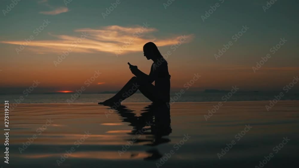 girl uses a smartphone at sunset by the ocean girl uses a smartphone at sunset by the ocean