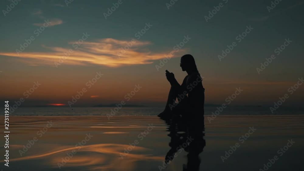 girl uses a smartphone at sunset by the ocean girl uses a smartphone at sunset by the ocean