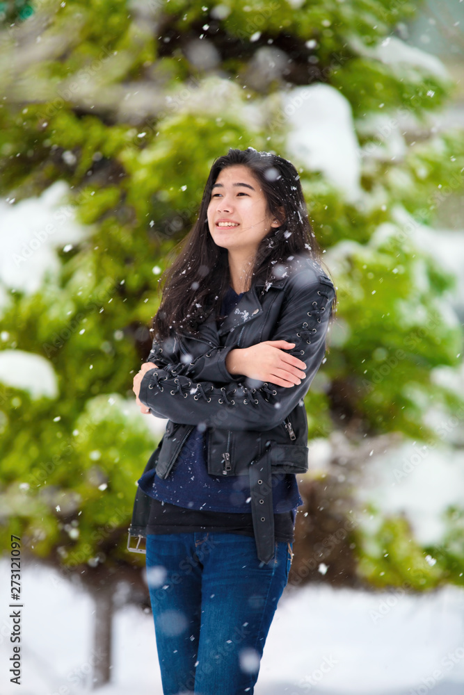 Teen girl standing outdoors in winter snowfall shivering from cold Teen girl standing outdoors in winter snowfall shivering from cold