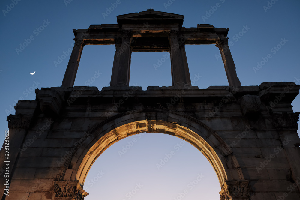 View of the Ruins of archway Hadrians Arch Temple Olympian Zeus Athens during sunset with moon in Athens in Greece - low light.