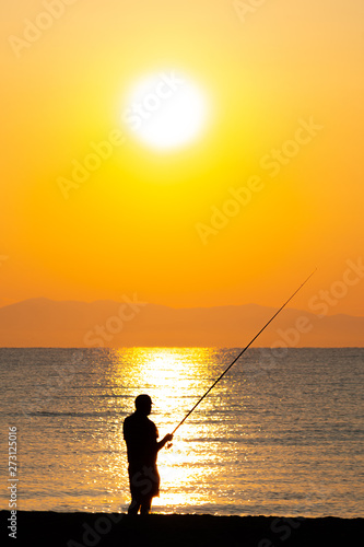 Silhouette of a man fishing at the beach in sunrise / sunset 