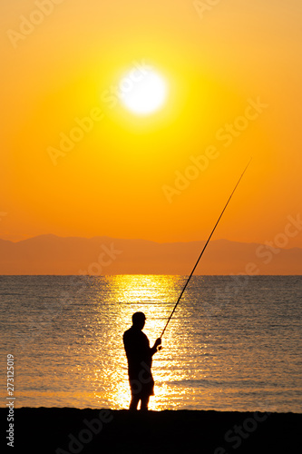 Silhouette of a man fishing at the beach in sunrise / sunset 