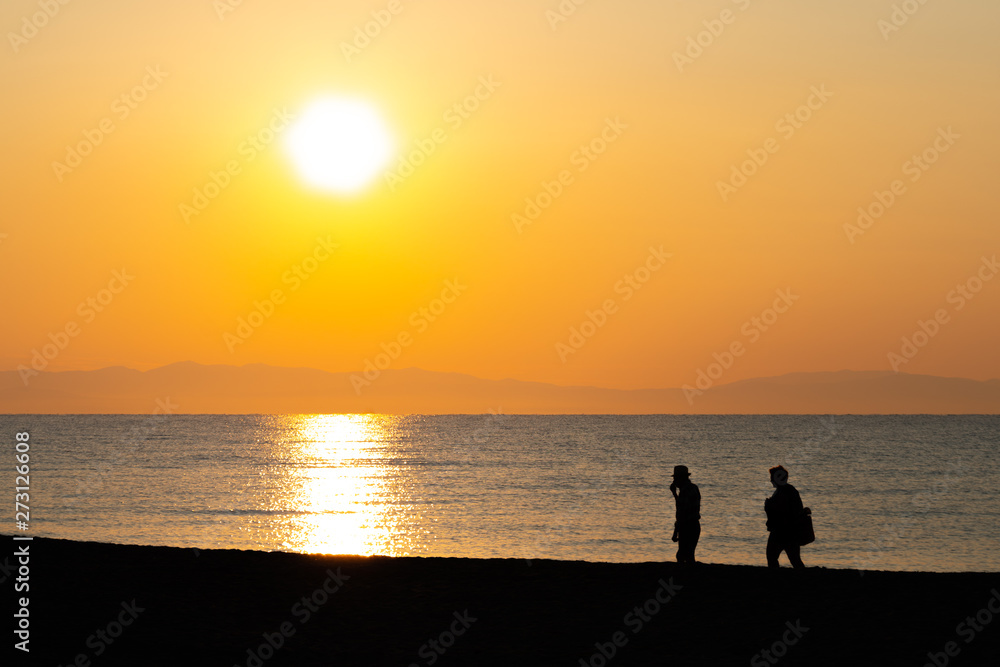 Silhouette of an elderly couple walking on the beach in sunrise / sunset on their vacation