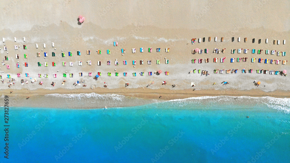 Aerial view of colorful chaise lounges (deck chairs) on the beach of the turquoise sea. Waves wash the shore. Top view.