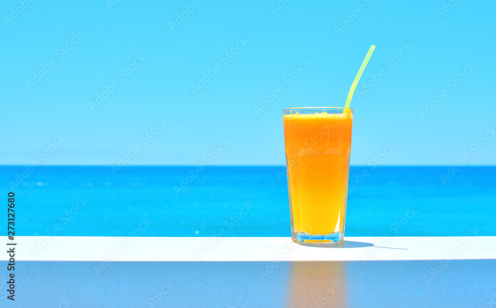 Orange fresh juice in a glass on the table with blue sea backdrop. Copy space. Orange fresh juice in a glass on the table with blue sea backdrop. Copy space.