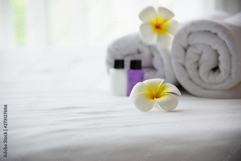 Hotel towel and shampoo and soap bath bottle set on white bed with plumeria flower decorated - relax vacation at the hotel resort concept Hotel towel and shampoo and soap bath bottle set on white bed with plumeria flower decorated - relax vacation at the hotel resort concept